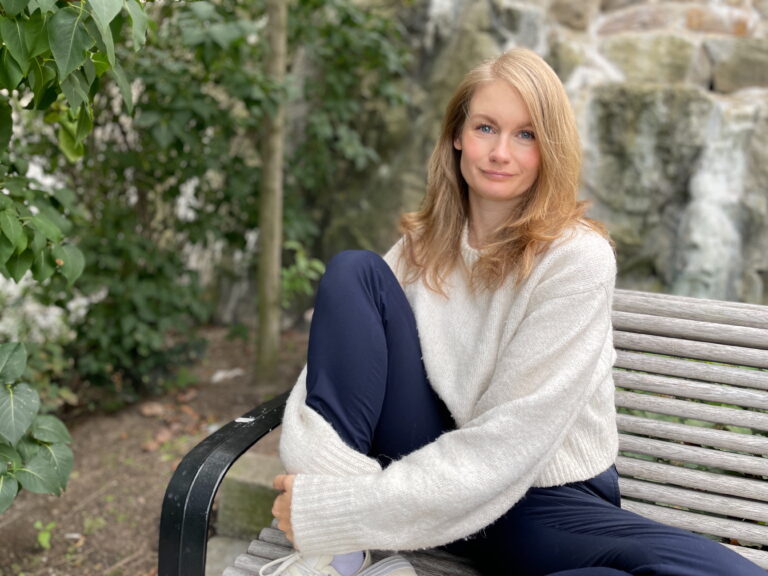 Josefine Berg sitter lugnt på en parkbänk i ljus stickad tröja