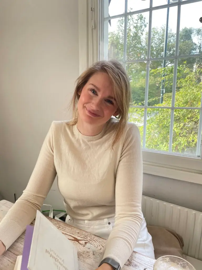 Josefine Berg sitter vid ett fönster i ljus tröja och ler